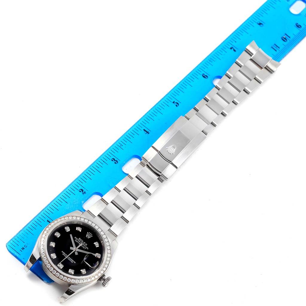 The image shows a top-down view of a Rolex Datejust 116244 Stainless Steel Black Dial 116244 Stainless Steel Black Dial watch laid next to a blue ruler, displaying its face and full metal bracelet.