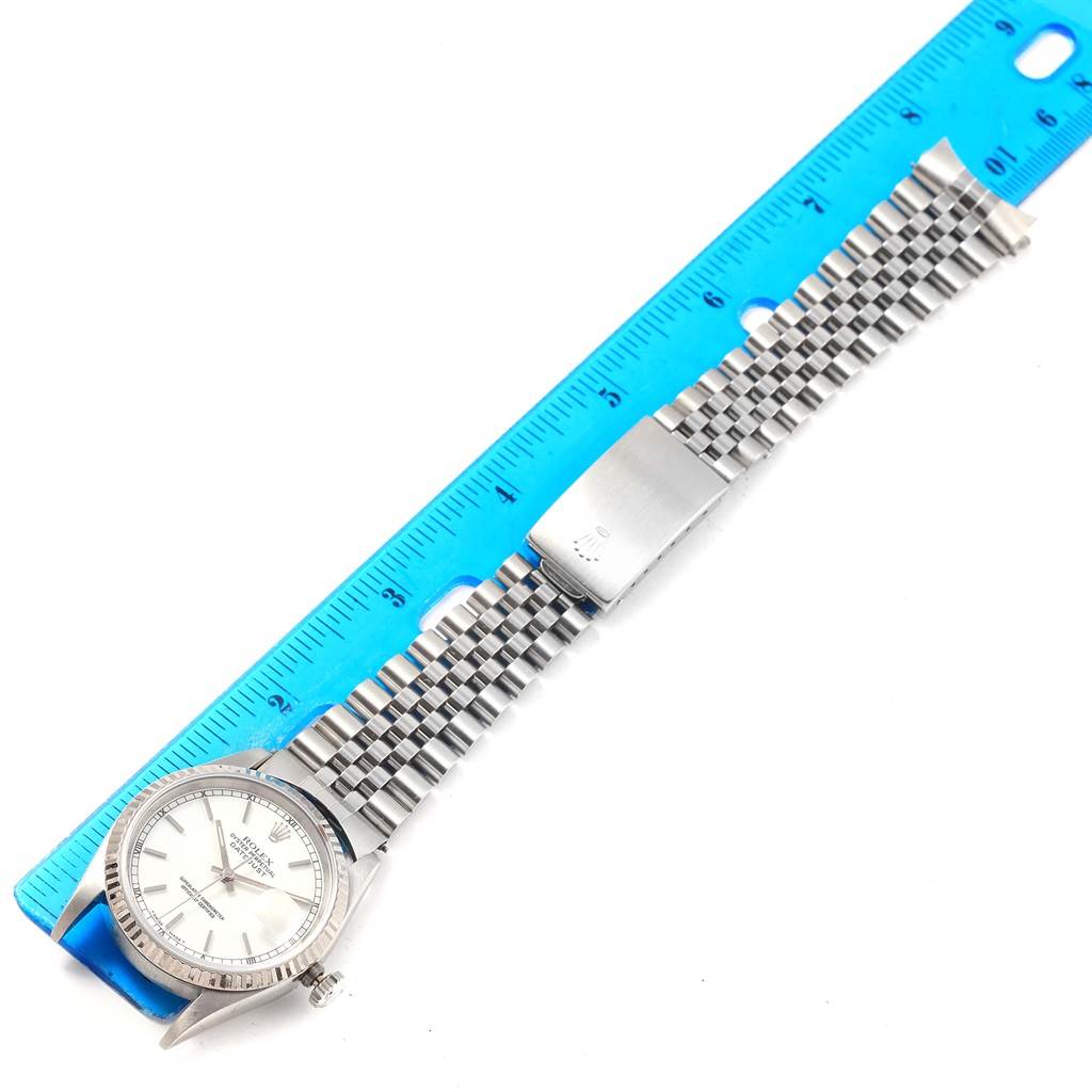 The Rolex Datejust 16234 Men's Stainless Steel White Dial 16234 Men's Stainless Steel White Dial watch is shown from an overhead angle, displaying the face, bezel, bracelet, and clasp next to a ruler.