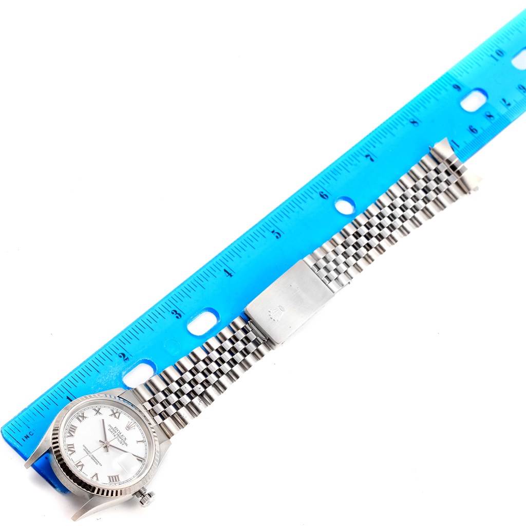 The Rolex Datejust 16234 Men's Stainless Steel White Dial 16234 Men's Stainless Steel White Dial watch is shown from a top-down angle, displaying the face, bracelet, and clasp next to a ruler.