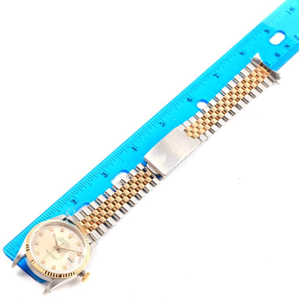 The image shows a Rolex Datejust 16233 Men's Steel and Gold (two tone) Silver Dial 16233 Men's Steel and Gold (two tone) Silver Dial watch lying flat with a blue ruler beside it, displaying the case, dial, and bracelet.