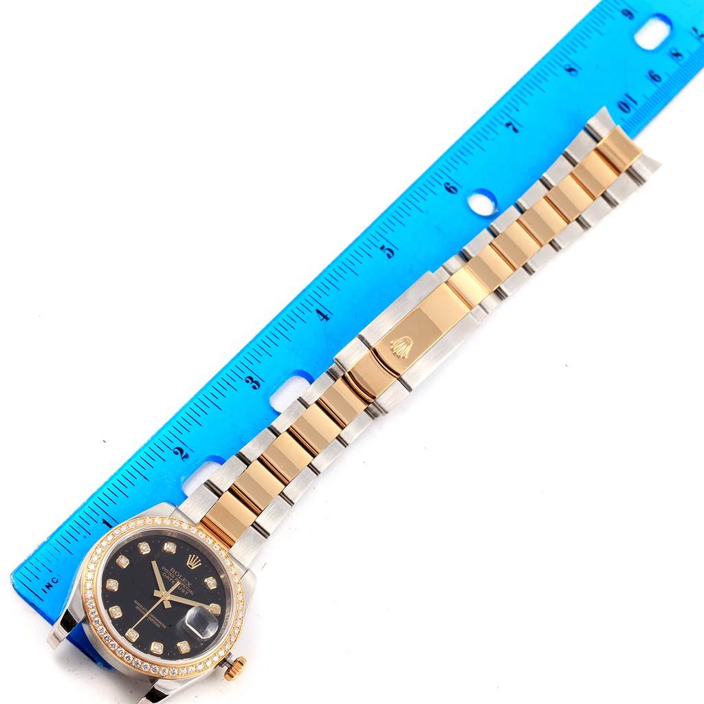 The Rolex Datejust 116243 Men
s Stainless Steel Black Dial 116243 Men
s Stainless Steel Black Dial watch is shown from above, displaying the face, bezel, and entire bracelet alongside a blue ruler.