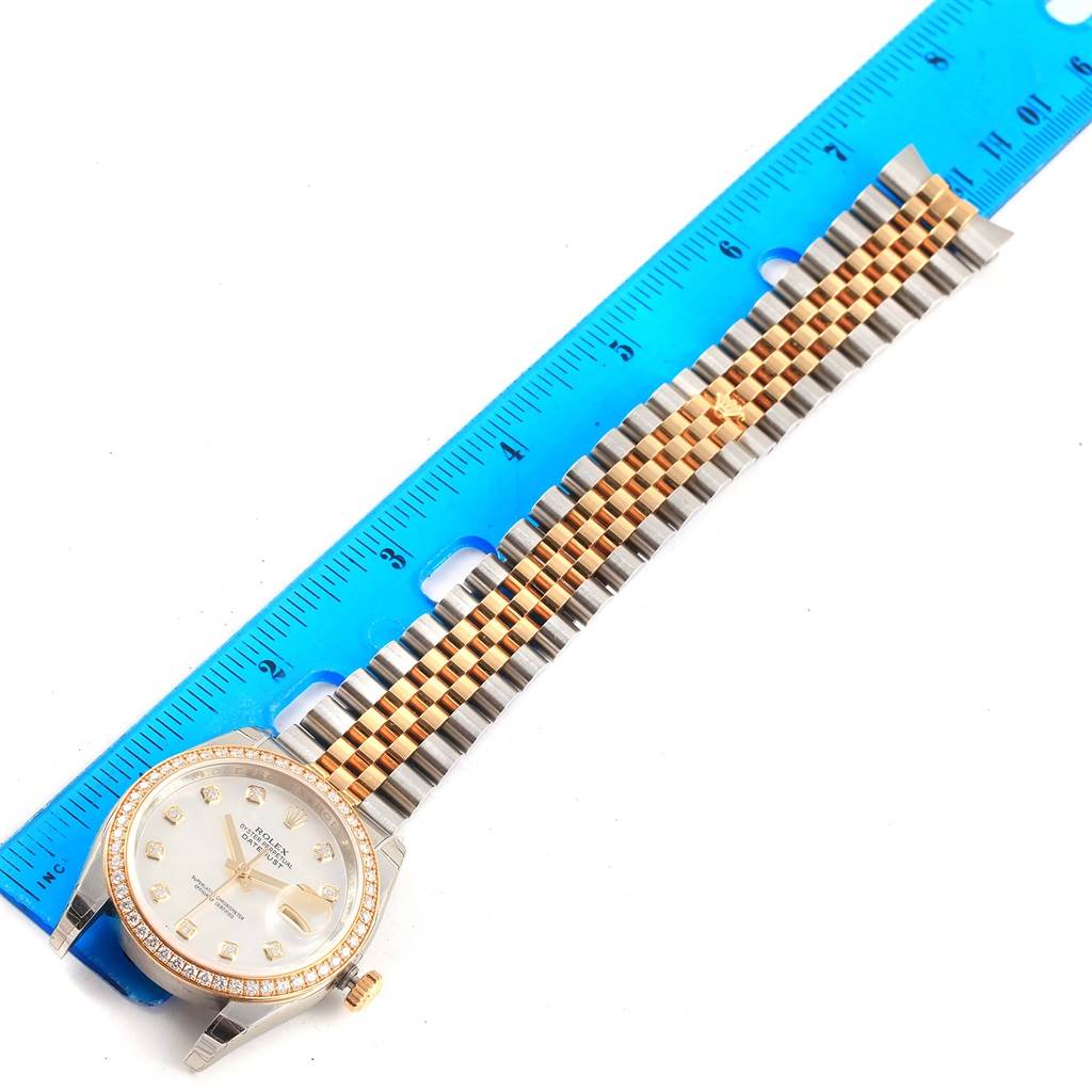 This image shows a Rolex Datejust 116243 Stainless Steel Mother of Pearl Dial 116243 Stainless Steel Mother of Pearl Dial watch laid flat with the face, crown, and band visible beside a blue measuring ruler.