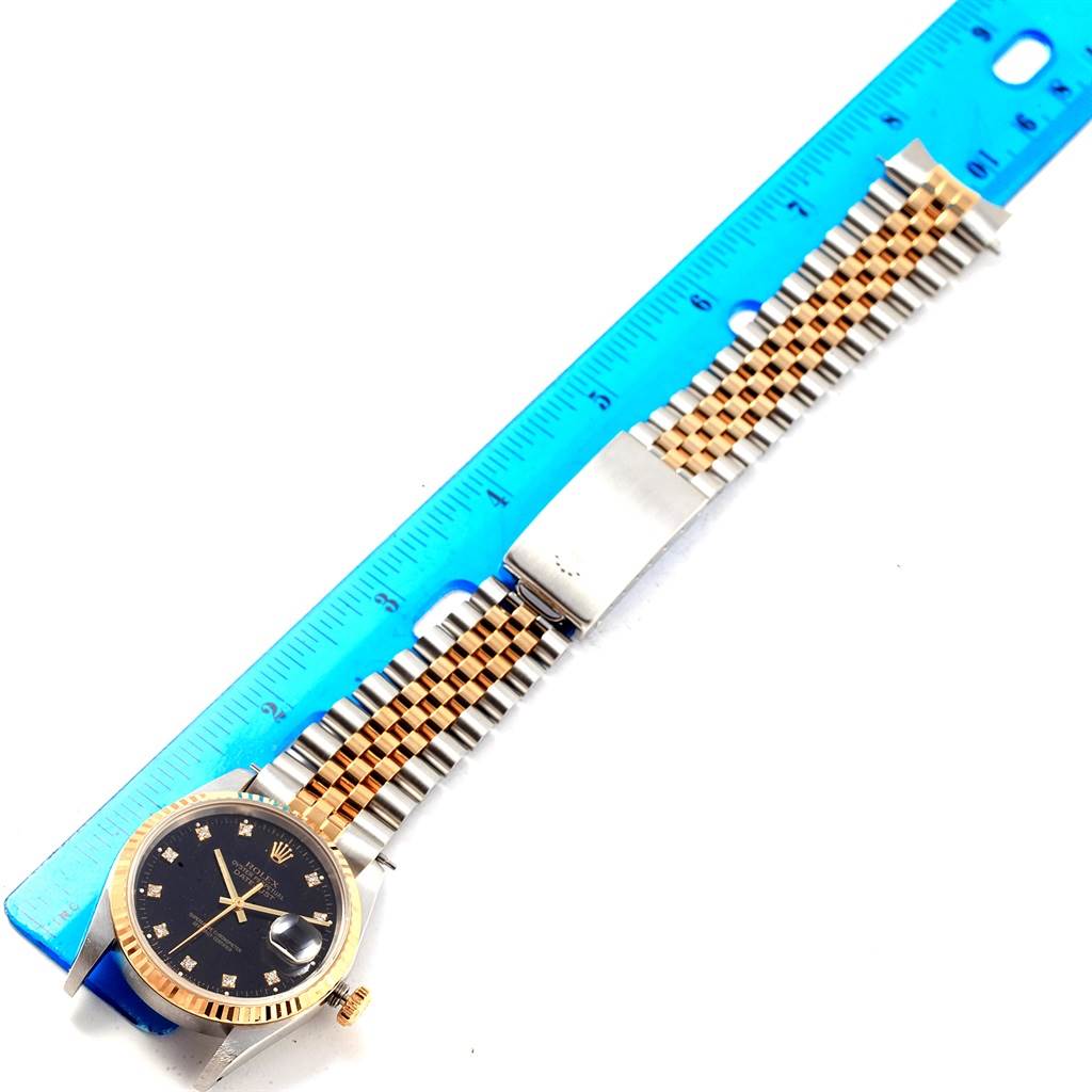 The image shows a Rolex Datejust 16233 Men's Steel and Gold (two tone) Black Dial 16233 Men's Steel and Gold (two tone) Black Dial watch laid flat with its bracelet alongside a blue ruler for measurement.