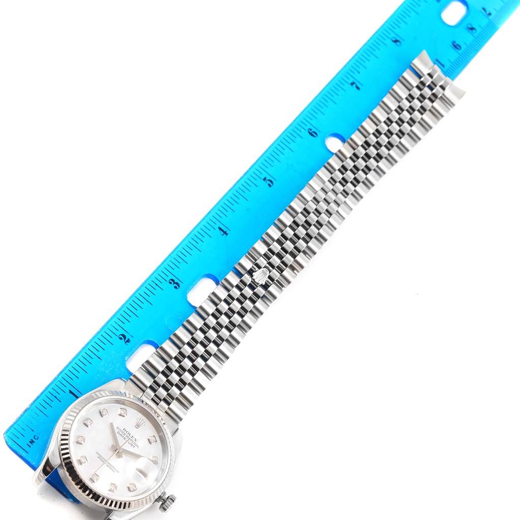 The image shows a top view of a Rolex Datejust 116234 Men
s Stainless Steel Mother of Pearl Dial 116234 Men
s Stainless Steel Mother of Pearl Dial watch, with a focus on its face and bracelet, alongside a blue ruler for scale.