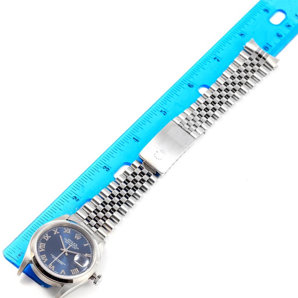 The image shows a top-down view of a Rolex Datejust 16200 Men's Stainless Steel Blue Dial 16200 Men's Stainless Steel Blue Dial watch with a blue dial and a silver jubilee bracelet, alongside a blue ruler for scale.