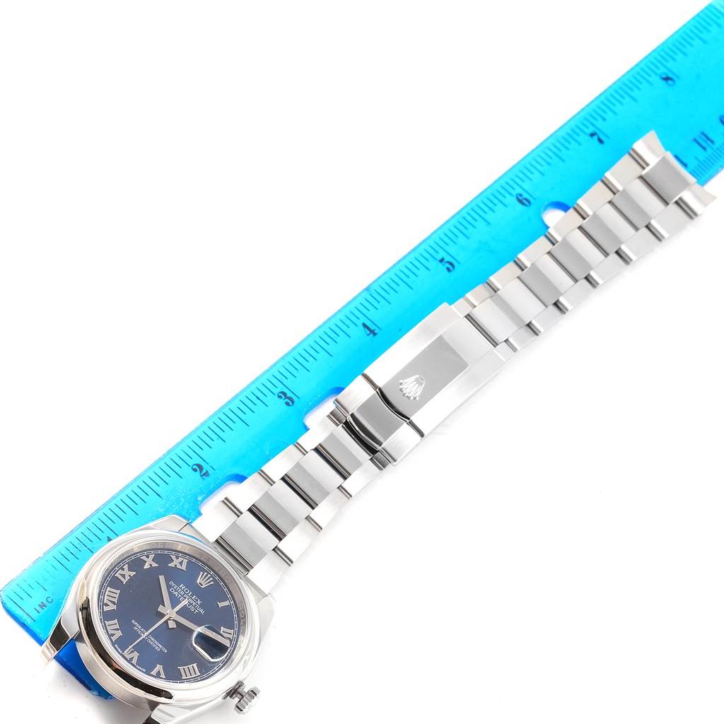 The Rolex Datejust 116200 Men's Stainless Steel Blue Dial 116200 Men's Stainless Steel Blue Dial watch is shown from a top-down angle, including the case, bracelet, and clasp, next to a ruler for scale.