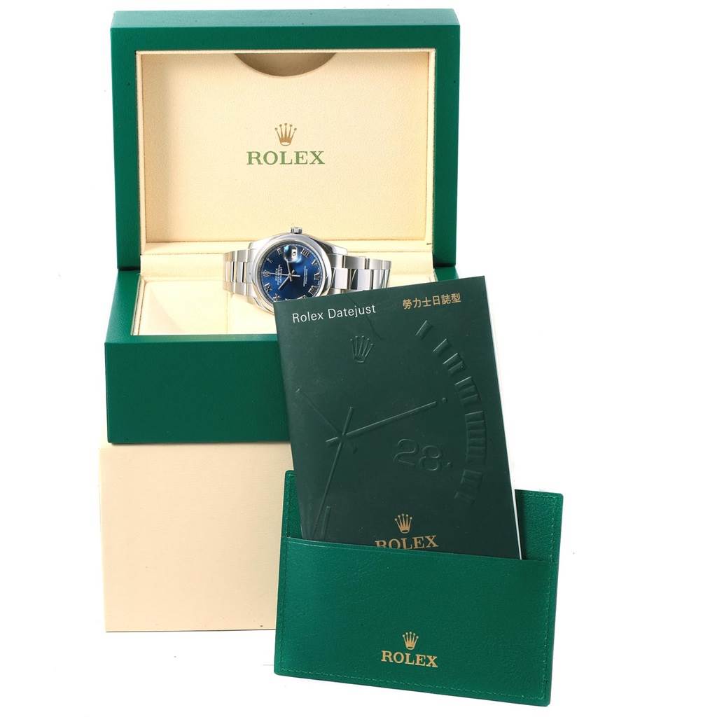 The Rolex Datejust 116200 Men's Stainless Steel Blue Dial 116200 Men's Stainless Steel Blue Dial watch is displayed inside its open box with a booklet and cardholder placed in front of the box.