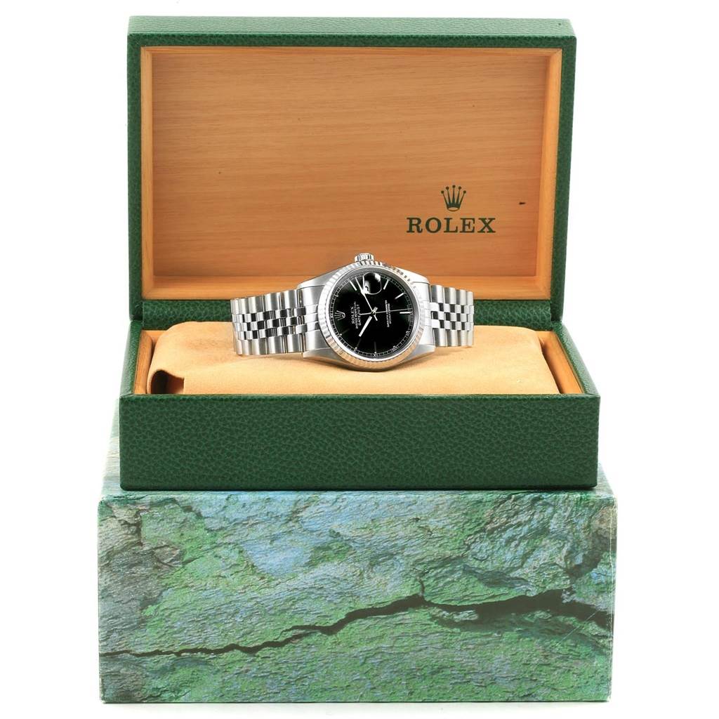 The Rolex Datejust 16234 Men's Stainless Steel Black Dial 16234 Men's Stainless Steel Black Dial watch is shown from the front, placed inside a green and orange display box with branding.