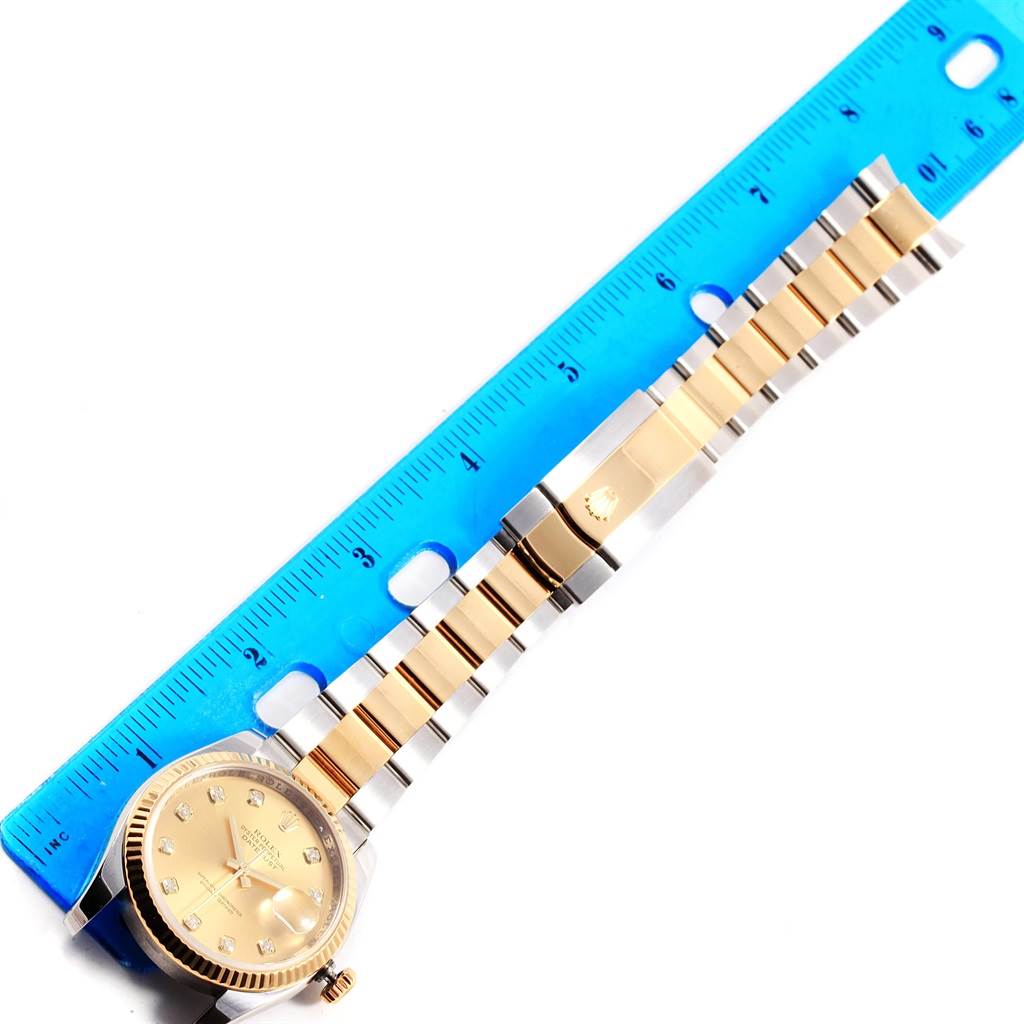 The Rolex Datejust 116233 Men's Stainless Steel Champagne Dial 116233 Men's Stainless Steel Champagne Dial watch is shown from an overhead angle, displaying the face, part of the bracelet, and clasp beside a ruler.