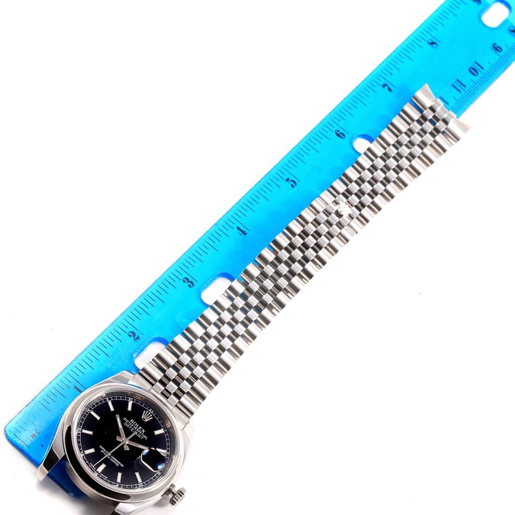 The image shows a Rolex Datejust 116200 Men's Stainless Steel Black Dial 116200 Men's Stainless Steel Black Dial watch laid flat next to a blue ruler, displaying the watch face, crown, and bracelet.