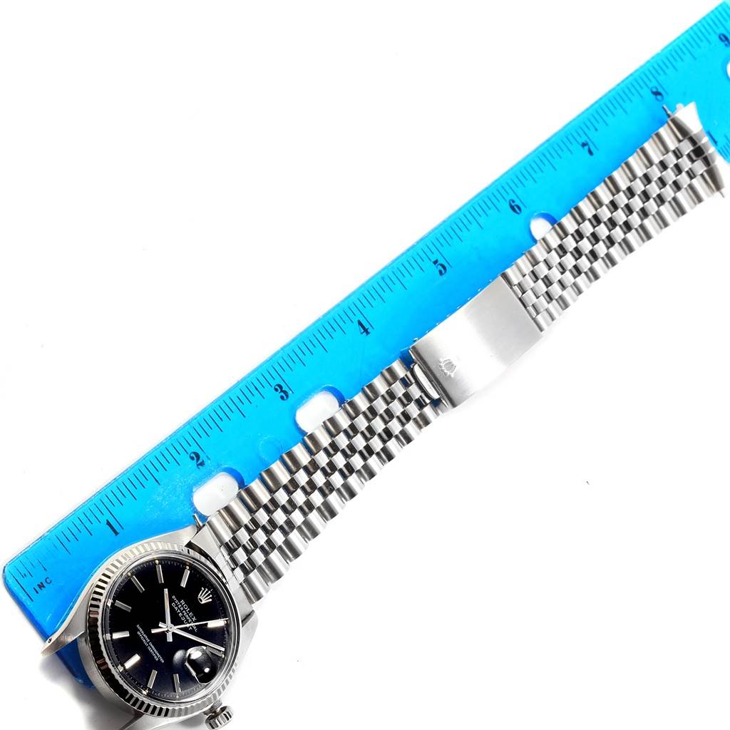 This image shows a Rolex Datejust 1601 Men's Stainless Steel Black Dial 1601 Men's Stainless Steel Black Dial watch laid flat with a blue ruler next to its stainless steel jubilee bracelet and clasp.