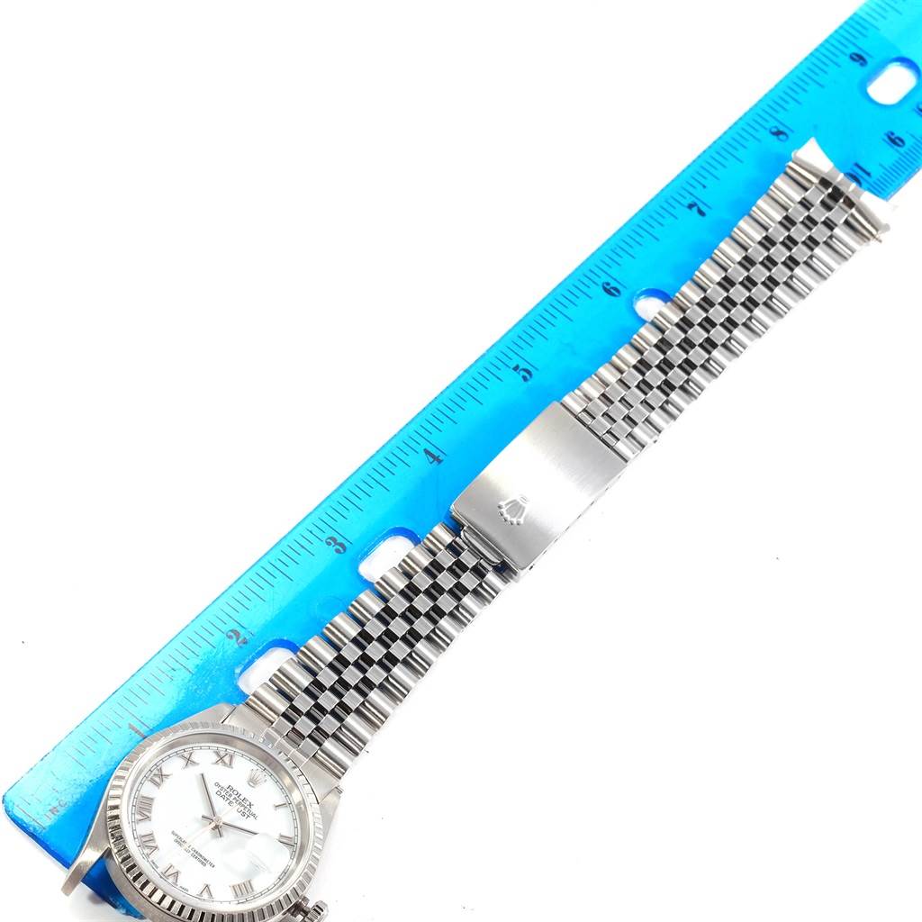 This image shows a Rolex Datejust 16220 Men
s Stainless Steel White Dial 16220 Men
s Stainless Steel White Dial watch laid flat with its face and woven metal strap visible, next to a blue ruler for scale.