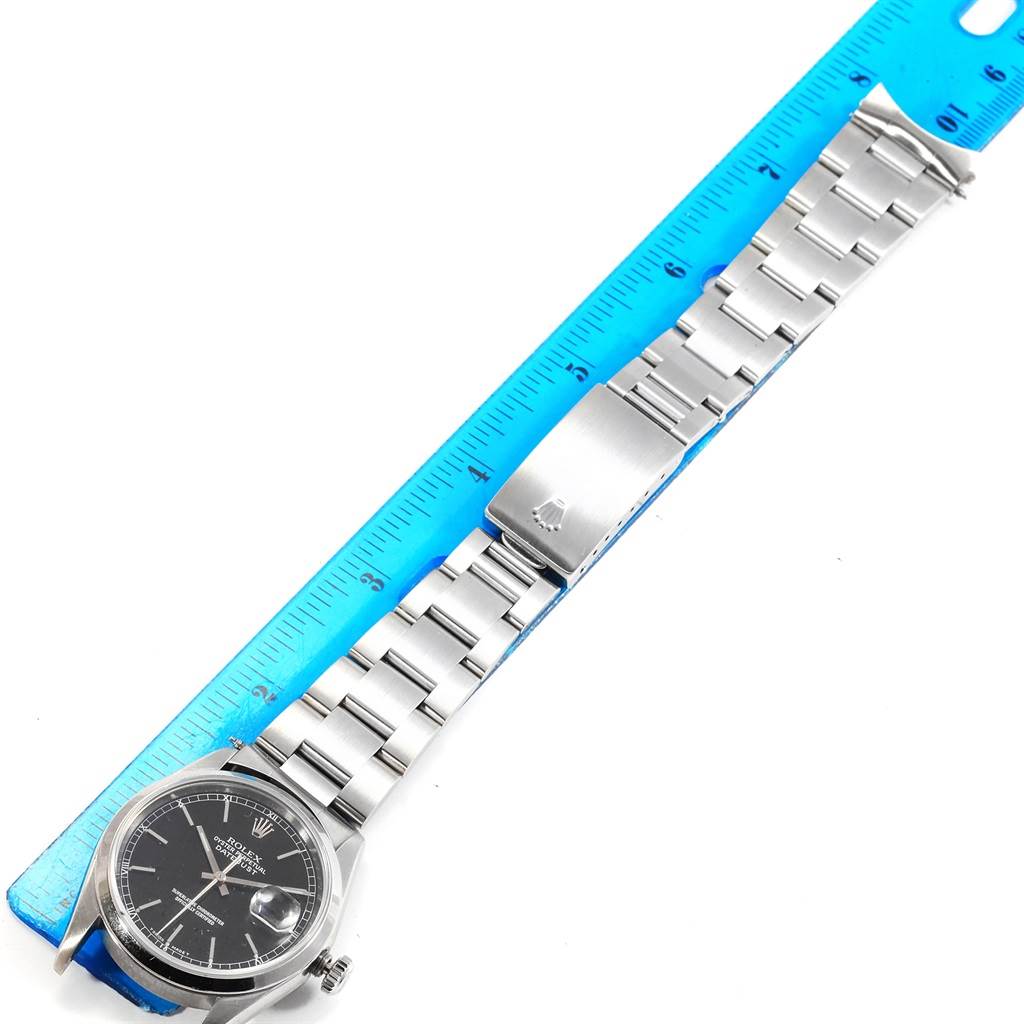 The image shows a Rolex Datejust 16200 Men's Stainless Steel Black Dial 16200 Men's Stainless Steel Black Dial watch, featured from a top-down angle, displaying the face, bracelet, and clasp against a blue ruler.