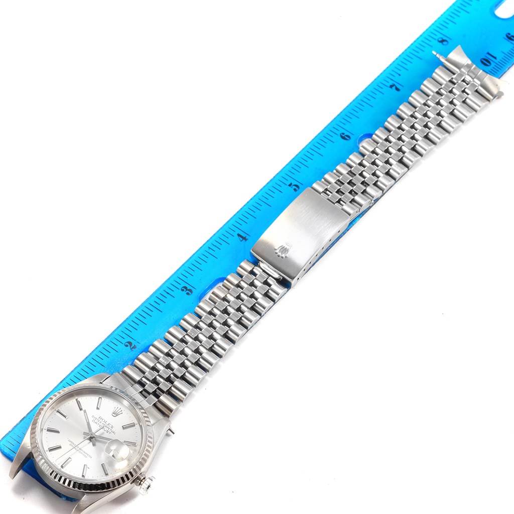 The image shows a top view of a Rolex Datejust 16234 Men's Stainless Steel Silver Dial 16234 Men's Stainless Steel Silver Dial watch next to a blue ruler, showcasing its dial, bezel, and metal bracelet.