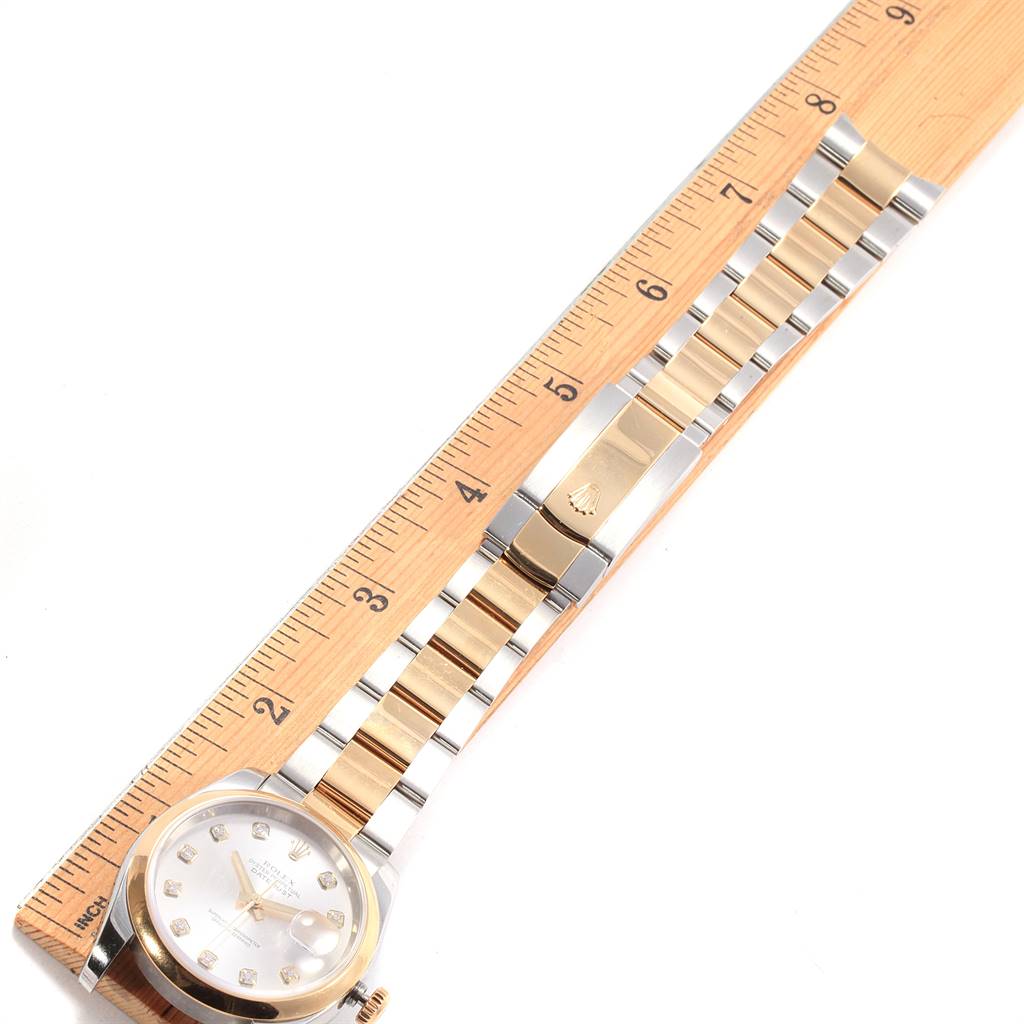 The Rolex Datejust 116203 Men's Steel and Gold (two tone) Silver Dial 116203 Men's Steel and Gold (two tone) Silver Dial watch is shown from an overhead angle, displaying the face and the bracelet beside a ruler.