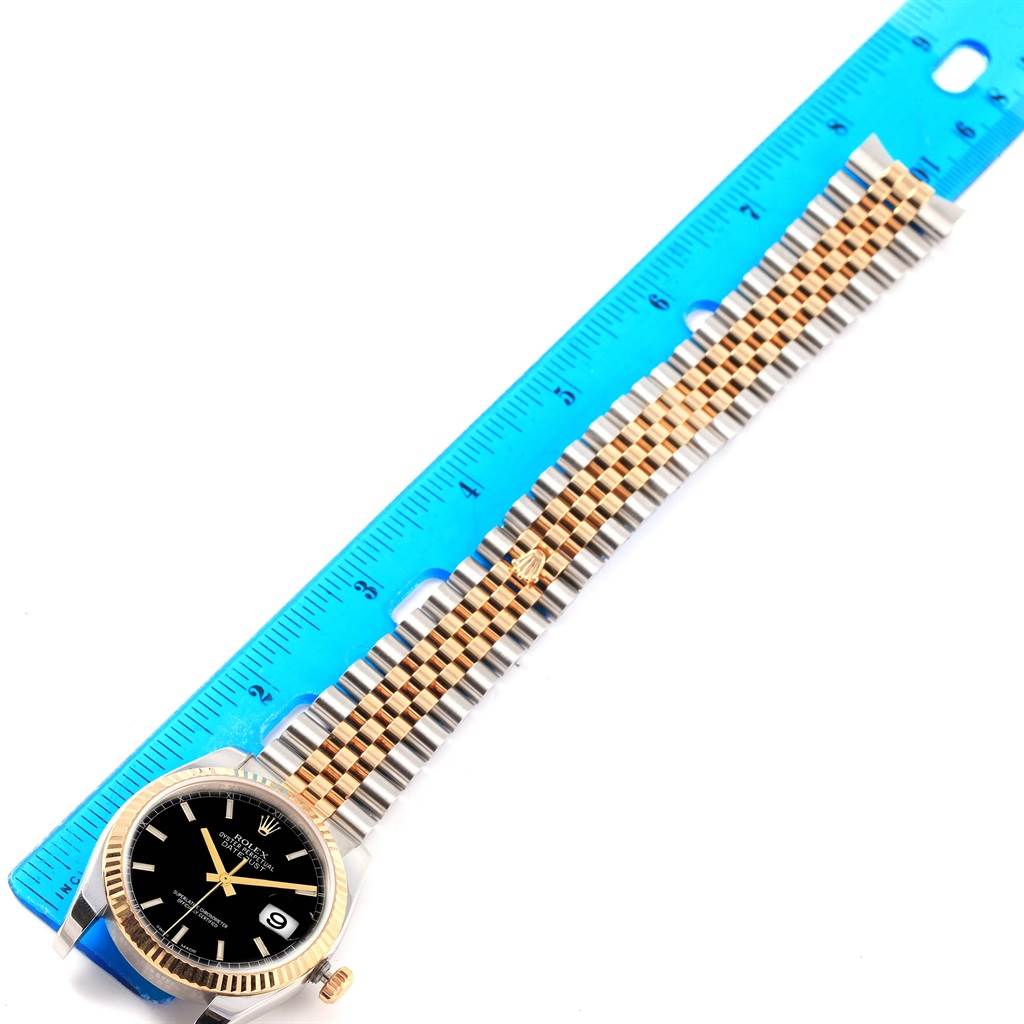 The Rolex Datejust 116233 Men's Stainless Steel Black Dial 116233 Men's Stainless Steel Black Dial watch is shown from a top-down angle alongside a ruler, displaying the face and bracelet.