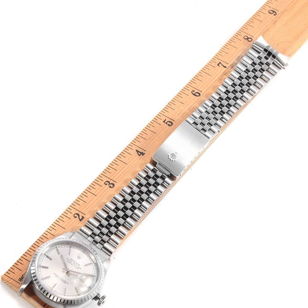 The Rolex Datejust 16220 Men
s Stainless Steel Silver Dial 16220 Men
s Stainless Steel Silver Dial watch is shown from a top-down angle, displaying the face, bezel, and bracelet on a ruler.