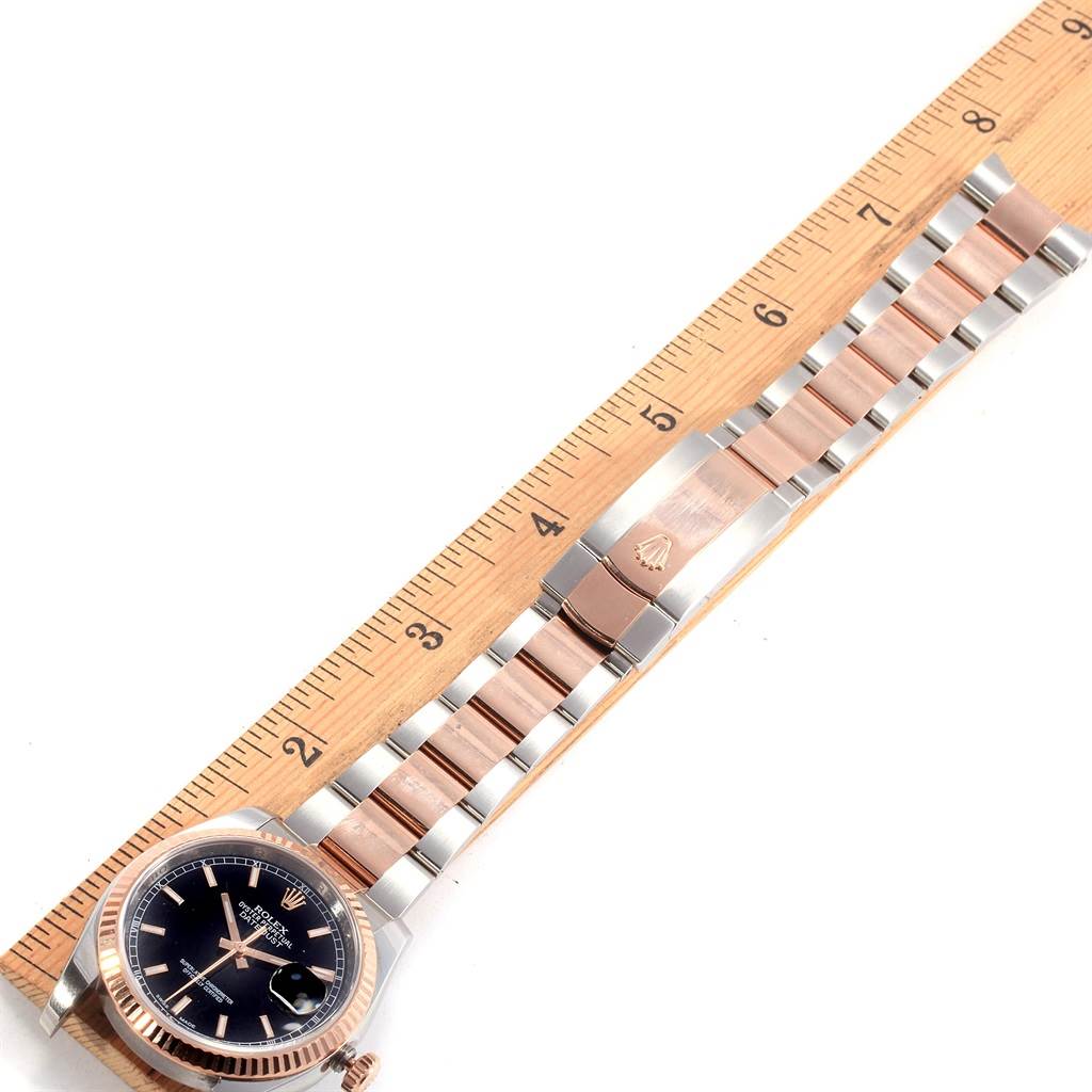 The image shows a Rolex Datejust 116231 Men's Steel and Gold (two tone) Black Dial 116231 Men's Steel and Gold (two tone) Black Dial watch laid flat, showcasing its face, bezel, and bracelet alongside a measurement ruler.