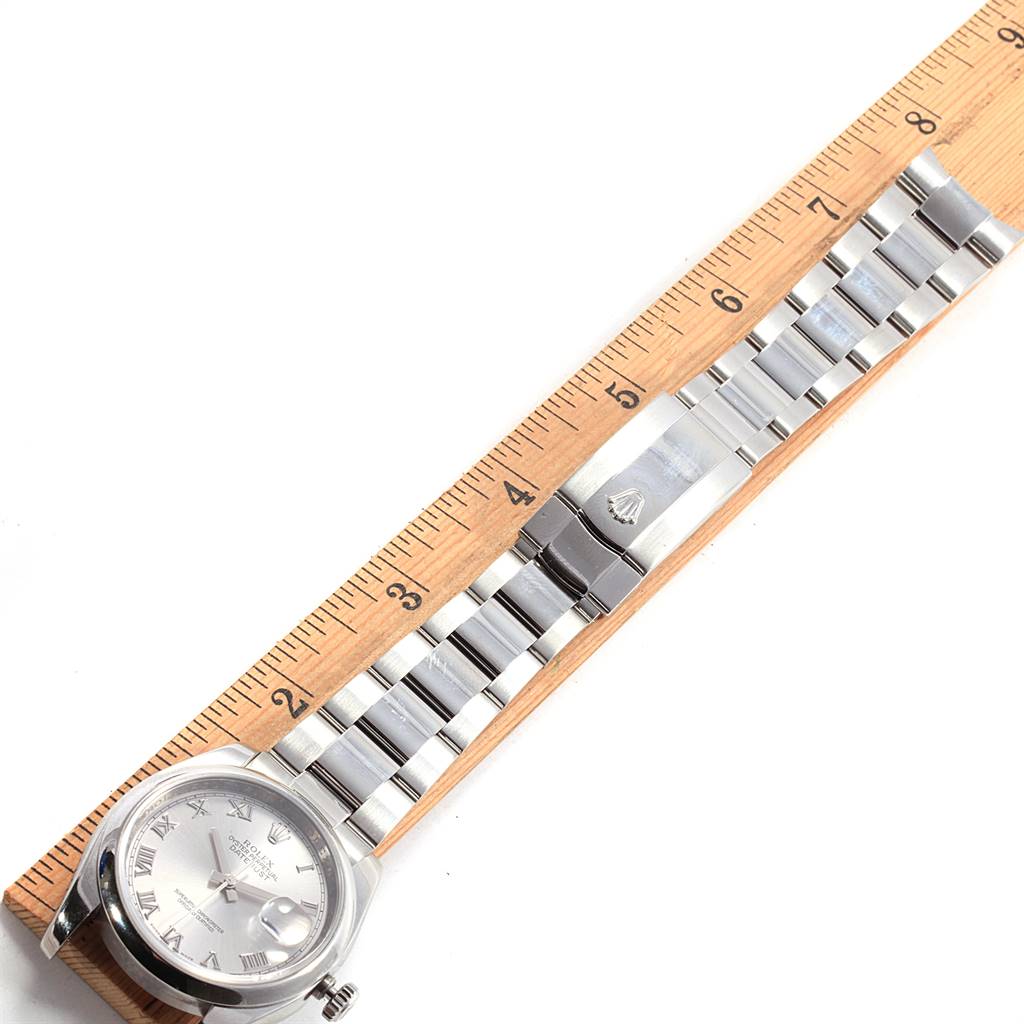 The image shows a top view of a Rolex Datejust 116200 Men's Stainless Steel Silver Dial 116200 Men's Stainless Steel Silver Dial watch, featuring its dial, bracelet, and clasp next to a measuring ruler.
