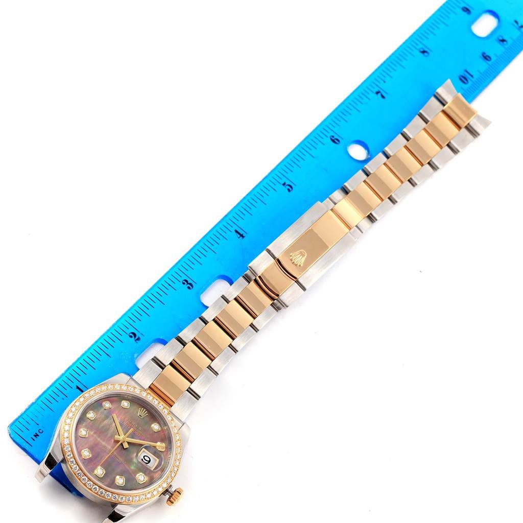 The image shows a Rolex Datejust 116243 Men's Stainless Steel Mother of Pearl Dial 116243 Men's Stainless Steel Mother of Pearl Dial watch laid flat adjacent to a ruler, highlighting the face and band.