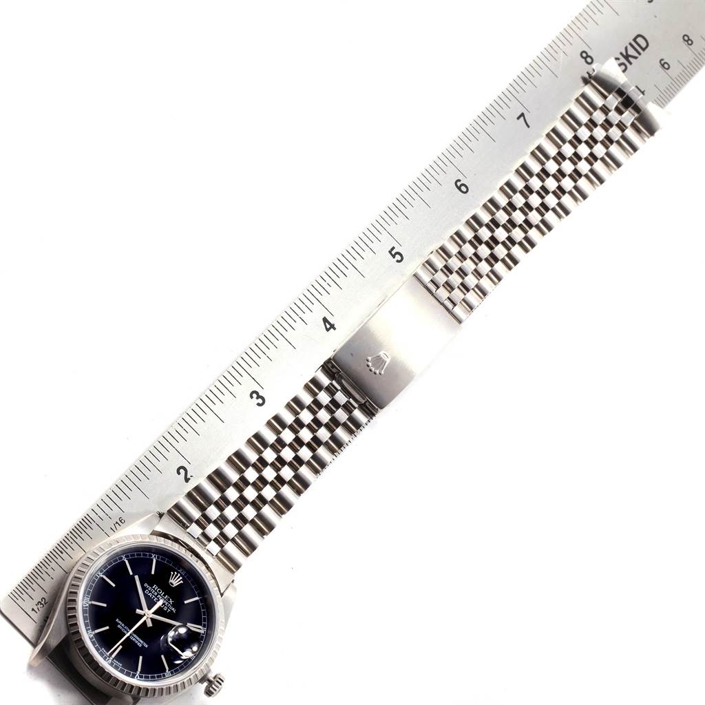 The image shows a top view of a Rolex Datejust 16220 Men
s Stainless Steel Black Dial 16220 Men
s Stainless Steel Black Dial watch with a metal band and clasp against a ruler.