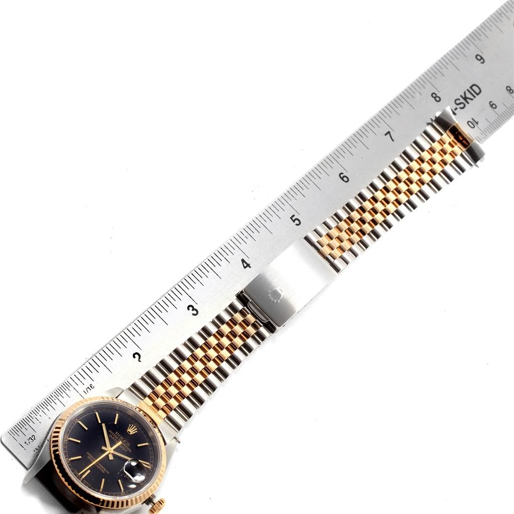 The Rolex Datejust 16233 Men's Steel and Gold (two tone) Black Dial 16233 Men's Steel and Gold (two tone) Black Dial watch is shown from a top-down angle, highlighting its face, bezel, and part of the bracelet with a ruler beside it.
