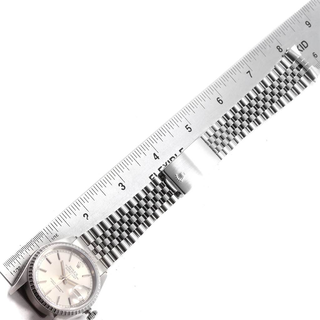 The Rolex Datejust 16220 Men
s Stainless Steel Silver Dial 16220 Men
s Stainless Steel Silver Dial watch is shown laid flat with a metal flexible ruler measuring its bracelet length.