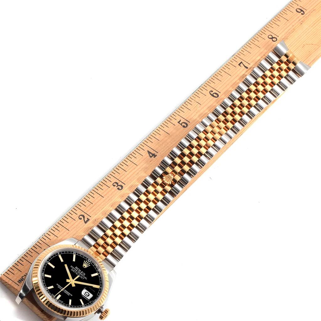 The Rolex Datejust 116233 Men's Stainless Steel Black Dial 116233 Men's Stainless Steel Black Dial watch is shown flat with face and full band, next to a ruler for measurement.