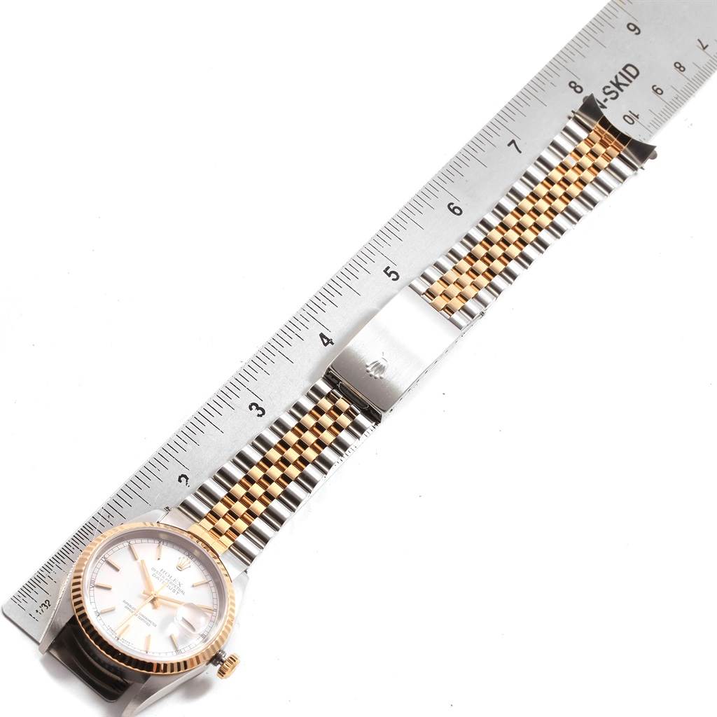 The Rolex Datejust 16233 Men's Steel and Gold (two tone) Silver Dial 16233 Men's Steel and Gold (two tone) Silver Dial watch is shown from a top view, displaying its face, crown, and two-tone bracelet beside a ruler.