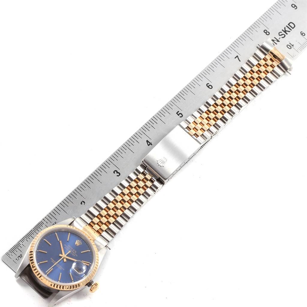 The image shows a Rolex Datejust 16233 Men
s Steel and Gold (two tone) Blue Dial 16233 Men
s Steel and Gold (two tone) Blue Dial watch laid flat with its two-tone bracelet and blue dial next to a ruler for scale.