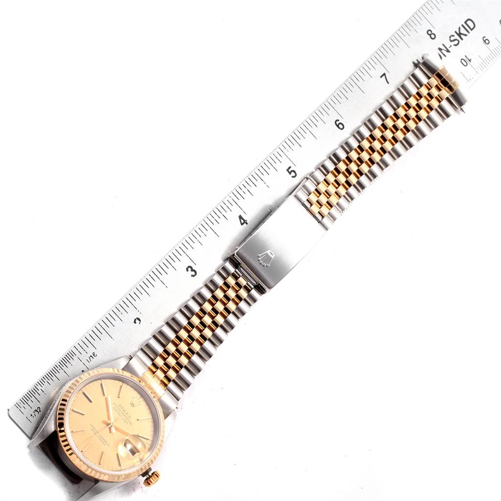 This image shows a Rolex Datejust 16233 Men
s Steel and Gold (two tone) Champagne Dial 16233 Men
s Steel and Gold (two tone) Champagne Dial watch with a partial view of its face, crown, and two-tone jubilee band next to a ruler.