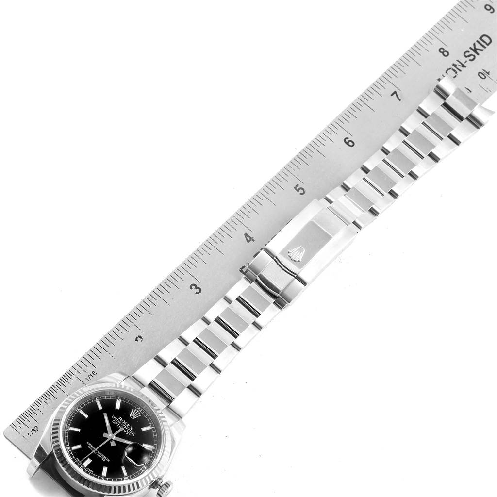 The image shows a Rolex Datejust 116234 Men
s Stainless Steel Black Dial 116234 Men
s Stainless Steel Black Dial watch laid flat with its bracelet and clasp fully extended alongside a ruler.