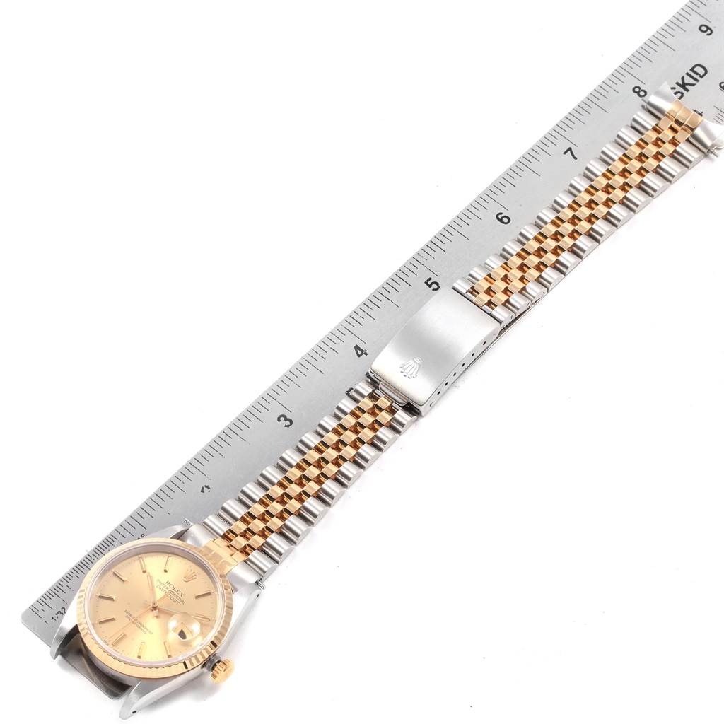 The image shows a Rolex Datejust 16233 Men
s Steel and Gold (two tone) Champagne Dial 16233 Men
s Steel and Gold (two tone) Champagne Dial watch laid flat, highlighting its gold dial and two-tone bracelet, alongside a measuring ruler.