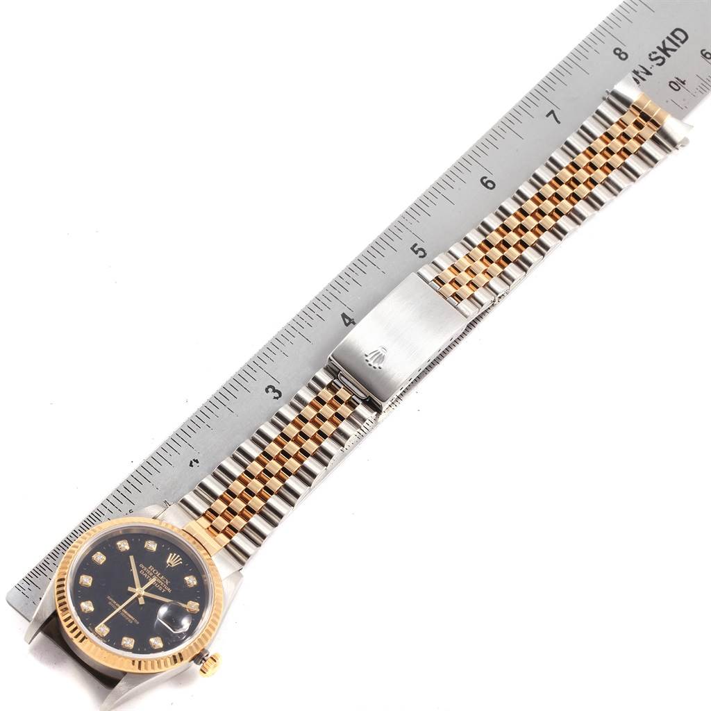 This image shows a Rolex Datejust 16233 Men's Steel and Gold (two tone) Black Dial 16233 Men's Steel and Gold (two tone) Black Dial watch with its face up, alongside a ruler for size reference.