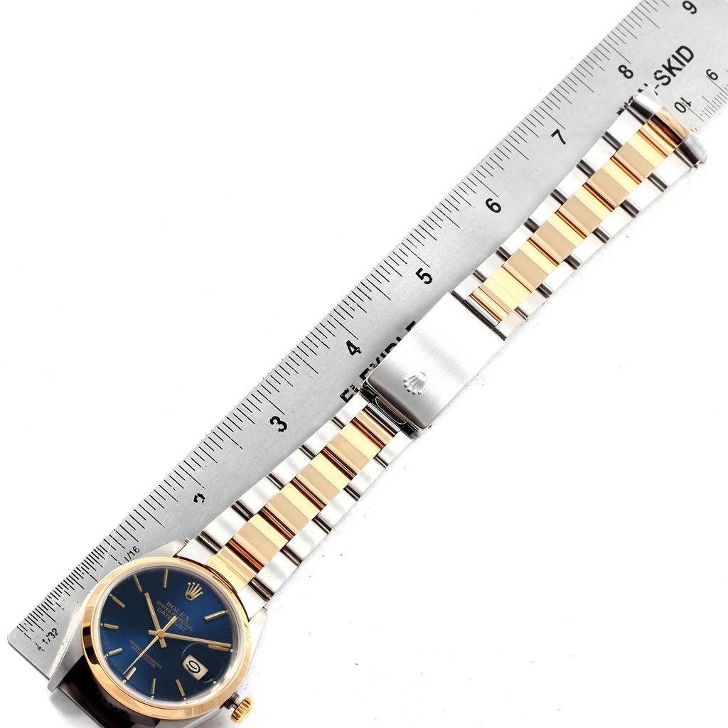 The Rolex Datejust 16203 Men's Steel and Gold (two tone) Blue Dial 16203 Men's Steel and Gold (two tone) Blue Dial watch is shown from a top view, displaying its face, band, and clasp alongside a ruler for scale.