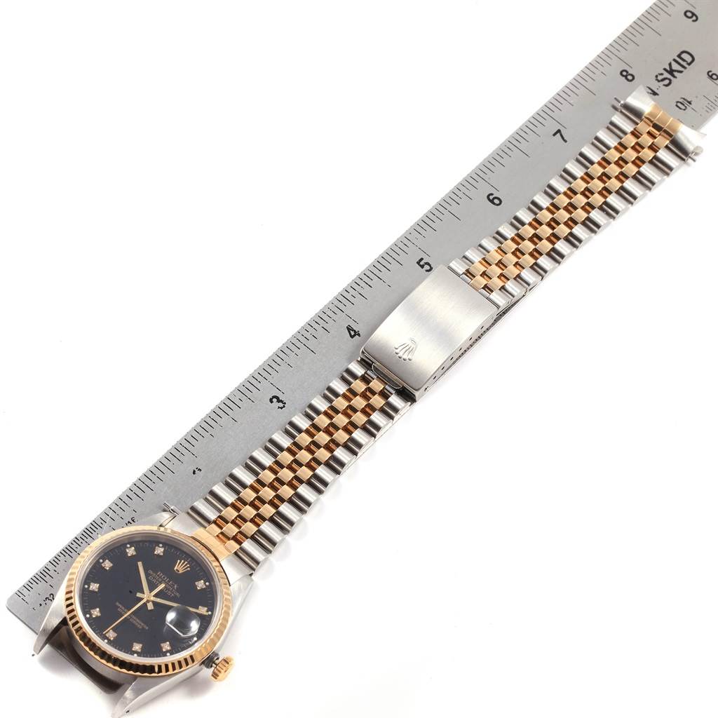 The image shows a top-down view of a Rolex Datejust 16233 Men
s Steel and Gold (two tone) Black Dial 16233 Men
s Steel and Gold (two tone) Black Dial watch, displaying the face, bezel, bracelet, and part of the clasp, next to a ruler.
