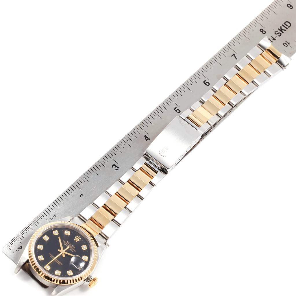 The Rolex Datejust 16233 Men
s Steel and Gold (two tone) Black Dial 16233 Men
s Steel and Gold (two tone) Black Dial watch is shown from a top-down angle, displaying the face, bracelet, and a ruler for measurement.
