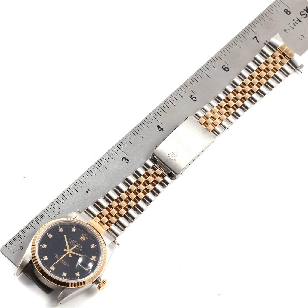 This image shows a Rolex Datejust 16233 Men's Steel and Gold (two tone) Black Dial 16233 Men's Steel and Gold (two tone) Black Dial watch lay flat beside a ruler, highlighting its face, bracelet, and clasp.