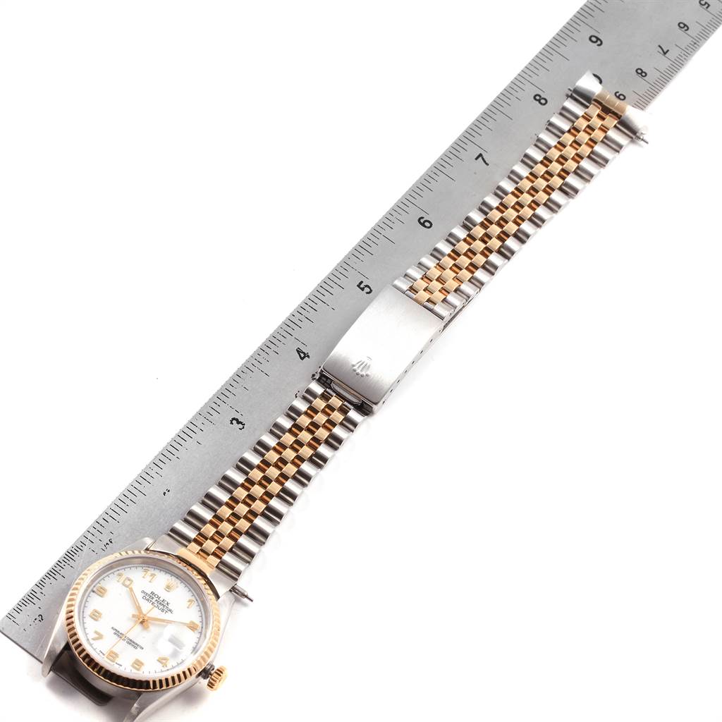This image shows a Rolex Datejust 16233 Men's Steel and Gold (two tone) White Dial 16233 Men's Steel and Gold (two tone) White Dial watch from an overhead angle, with its bracelet extended next to a ruler.