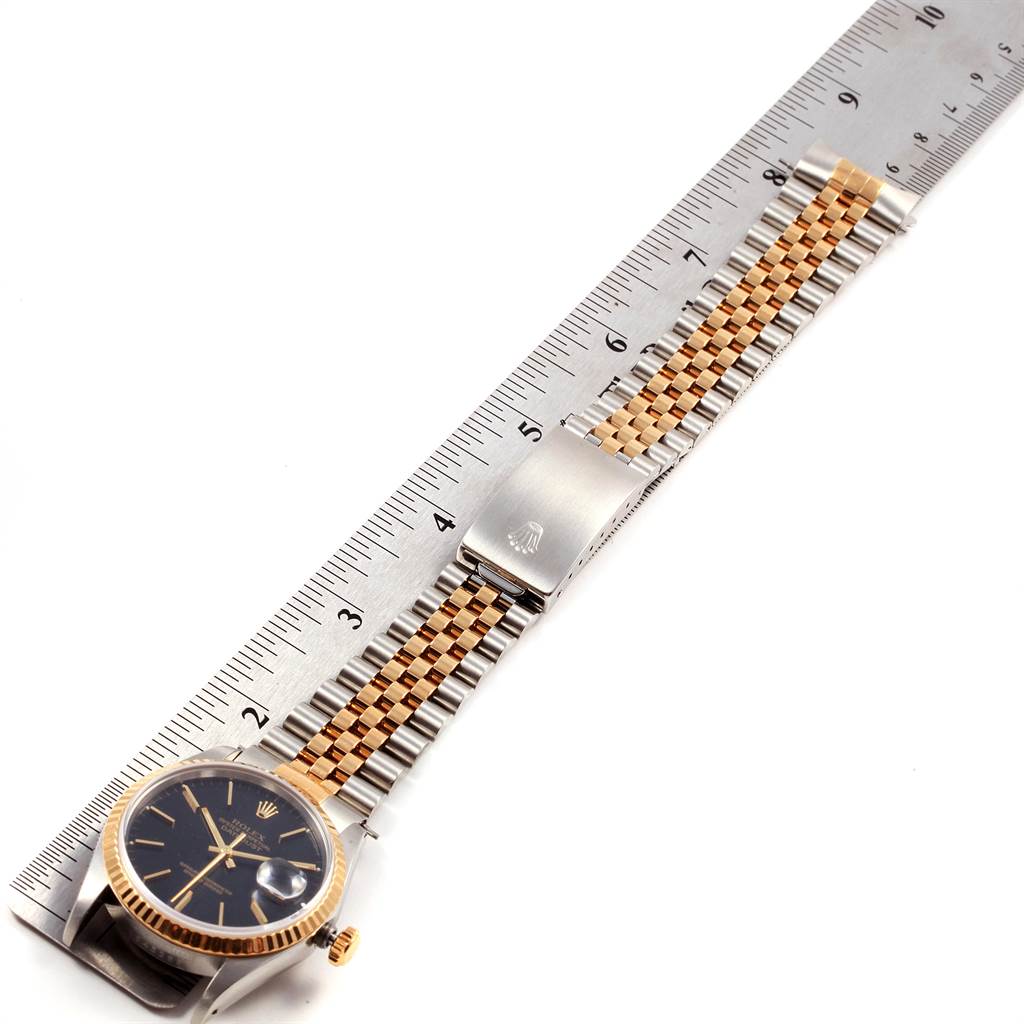 The Rolex Datejust 16233 Men's Steel and Gold (two tone) Black Dial 16233 Men's Steel and Gold (two tone) Black Dial watch is shown flat with its bracelet extended alongside a ruler for measurement.