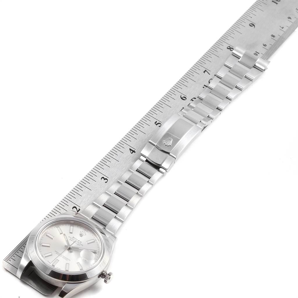 The image displays a Rolex Datejust 116300 Men
s Stainless Steel Silver Dial 116300 Men
s Stainless Steel Silver Dial watch laid flat next to a ruler, showing the face, bezel, bracelet, and clasp.