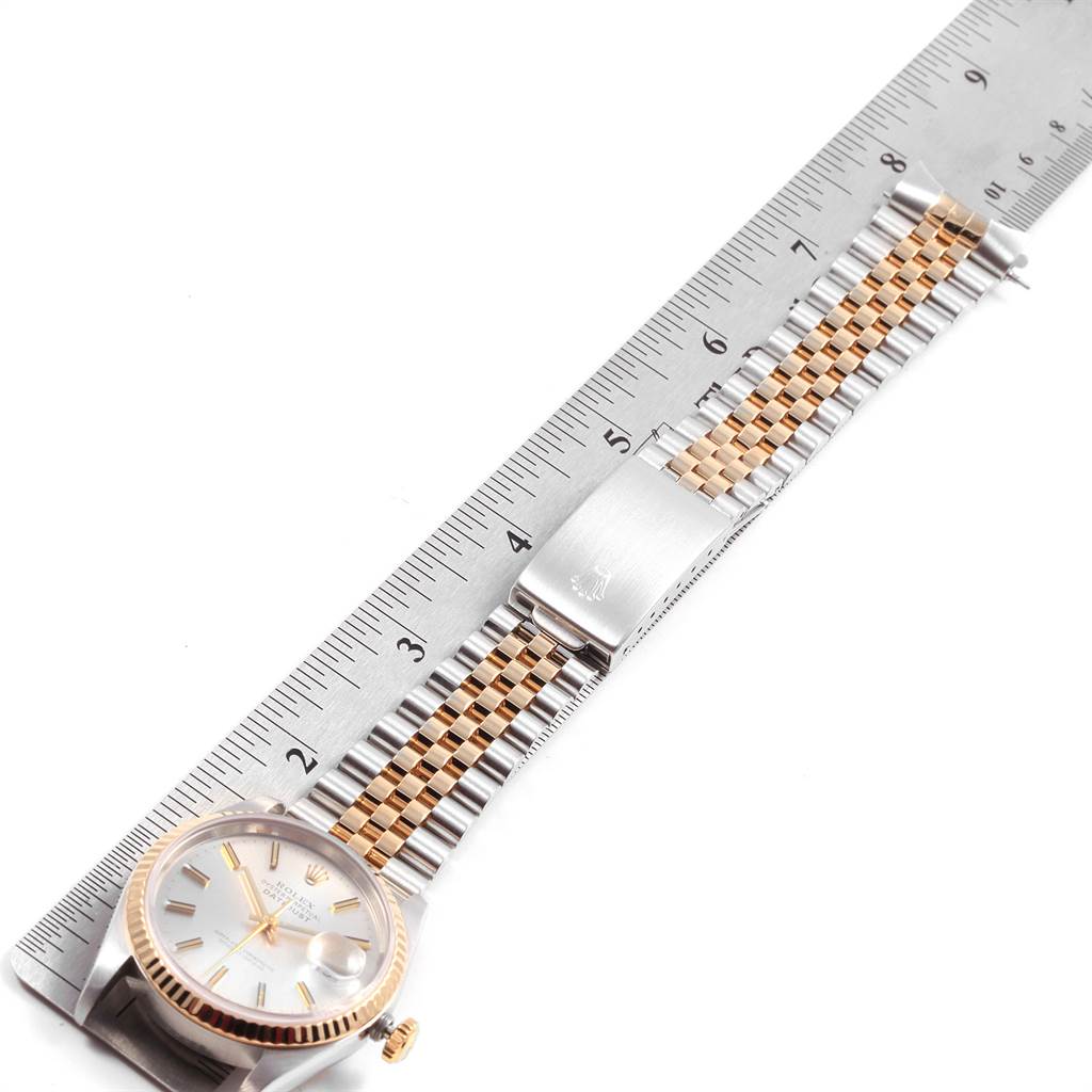 The image shows a Rolex Datejust 16233 Men's Steel and Gold (two tone) Silver Dial 16233 Men's Steel and Gold (two tone) Silver Dial watch at a top-down angle, highlighting the face, crown, and two-tone bracelet next to a ruler.