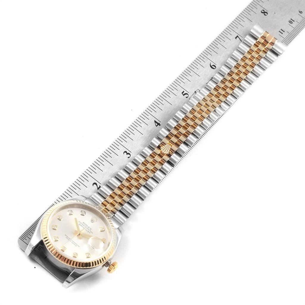 The image shows a top view of a Rolex Datejust 116233 Men
s Stainless Steel Silver Dial 116233 Men
s Stainless Steel Silver Dial watch with a silver and gold jubilee bracelet next to a ruler.