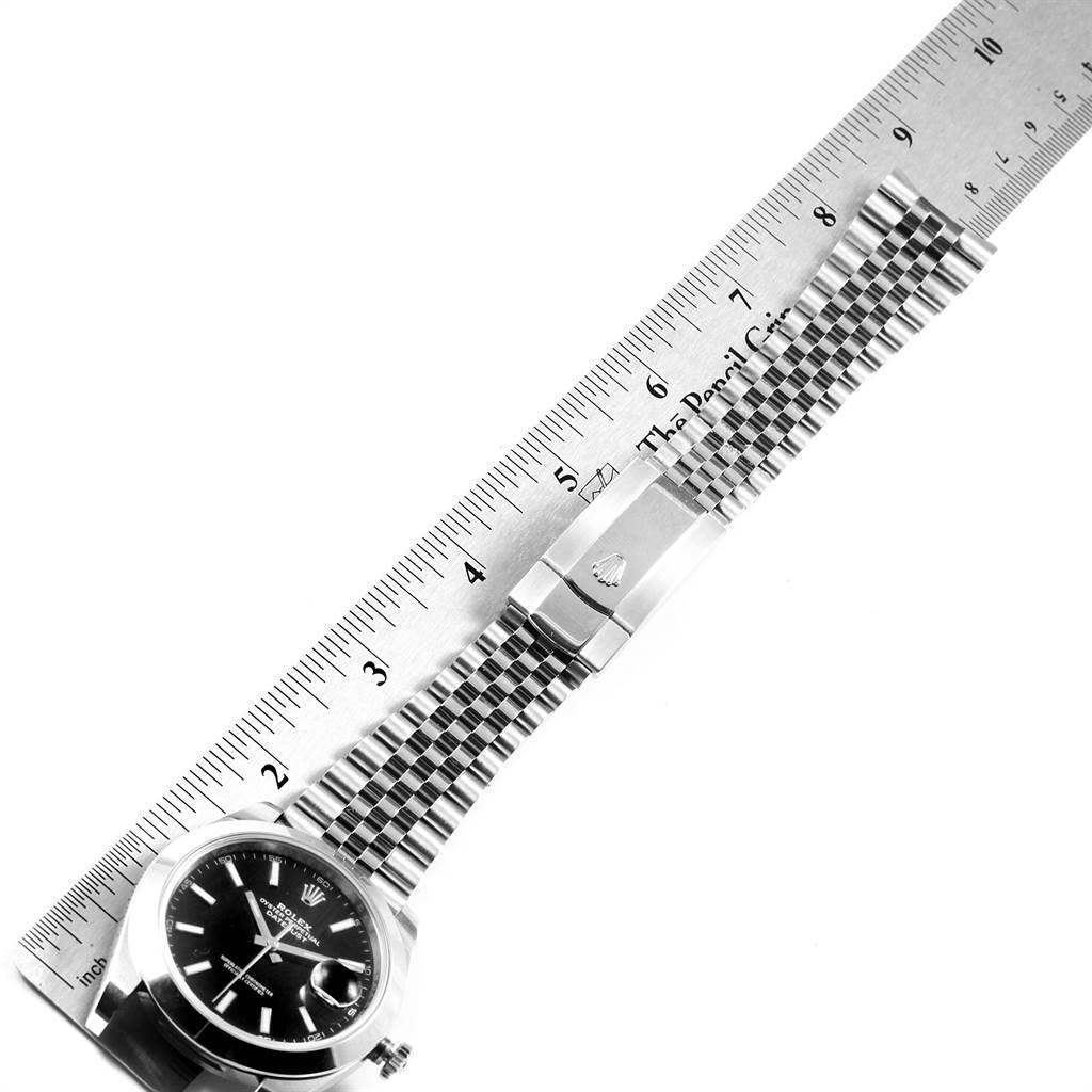 The Rolex Datejust 126300 Men
s Stainless Steel Black Dial 126300 Men
s Stainless Steel Black Dial watch is shown from a top-down angle, highlighting its dial, bracelet, and clasp alongside a ruler.