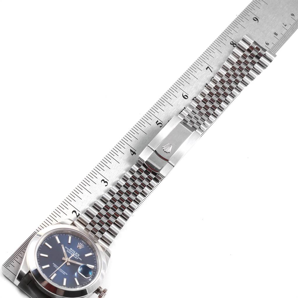 The image shows a Rolex Datejust 126300 Men
s Stainless Steel Blue Dial 126300 Men
s Stainless Steel Blue Dial watch laid flat with the face, bracelet, and clasp visible, positioned next to a ruler for scale.