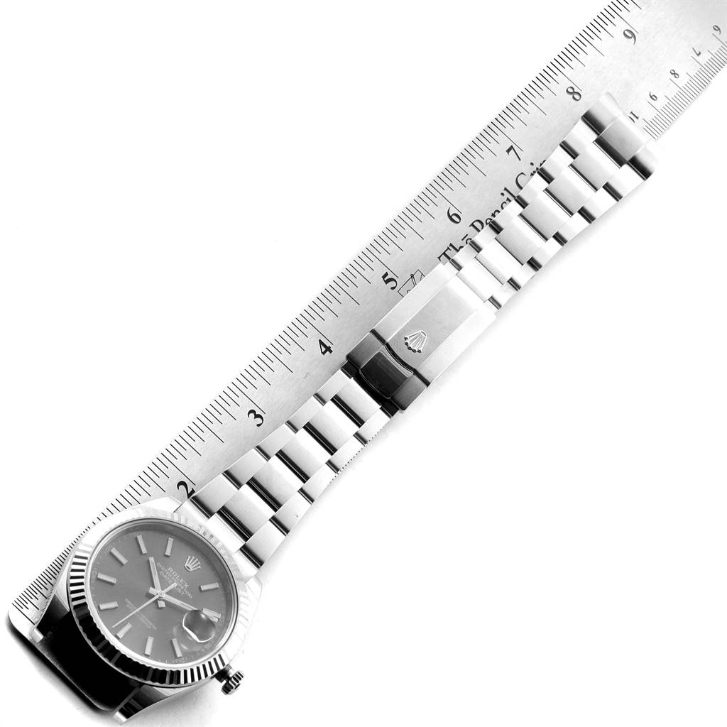 The Rolex Datejust 126334 Men
s Stainless Steel Grey Dial 126334 Men
s Stainless Steel Grey Dial watch is shown from a top-down angle with its dial, bracelet, and clasp visible next to a ruler.
