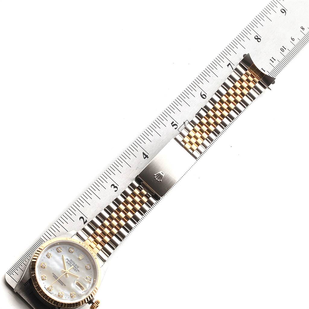 The Rolex Datejust 16233 Men's Steel and Gold (two tone) Mother of Pearl Dial 16233 Men's Steel and Gold (two tone) Mother of Pearl Dial watch is shown flat with its face, crown, and full bracelet next to a ruler.