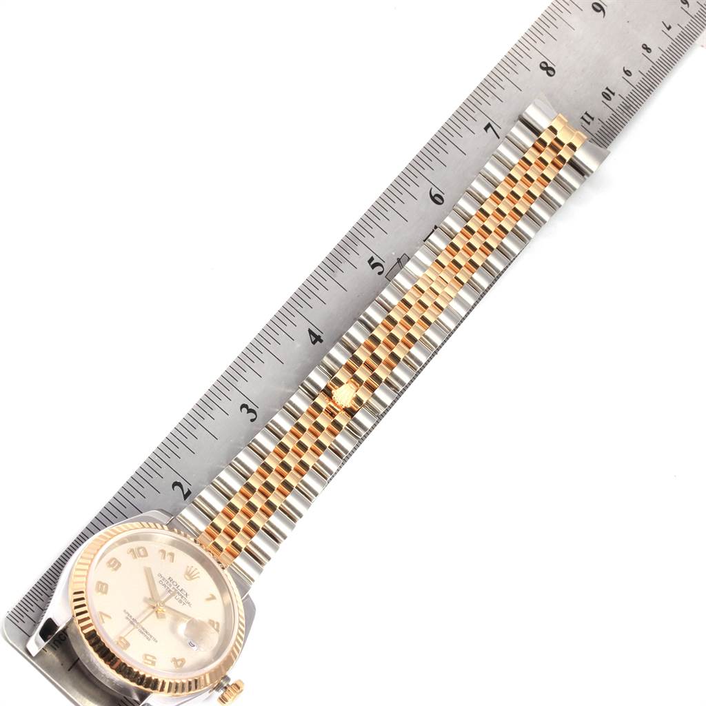 This image shows a top view of a Rolex Datejust 116233 Men's Stainless Steel Beige Dial 116233 Men's Stainless Steel Beige Dial watch and its gold and silver jubilee bracelet alongside a ruler.