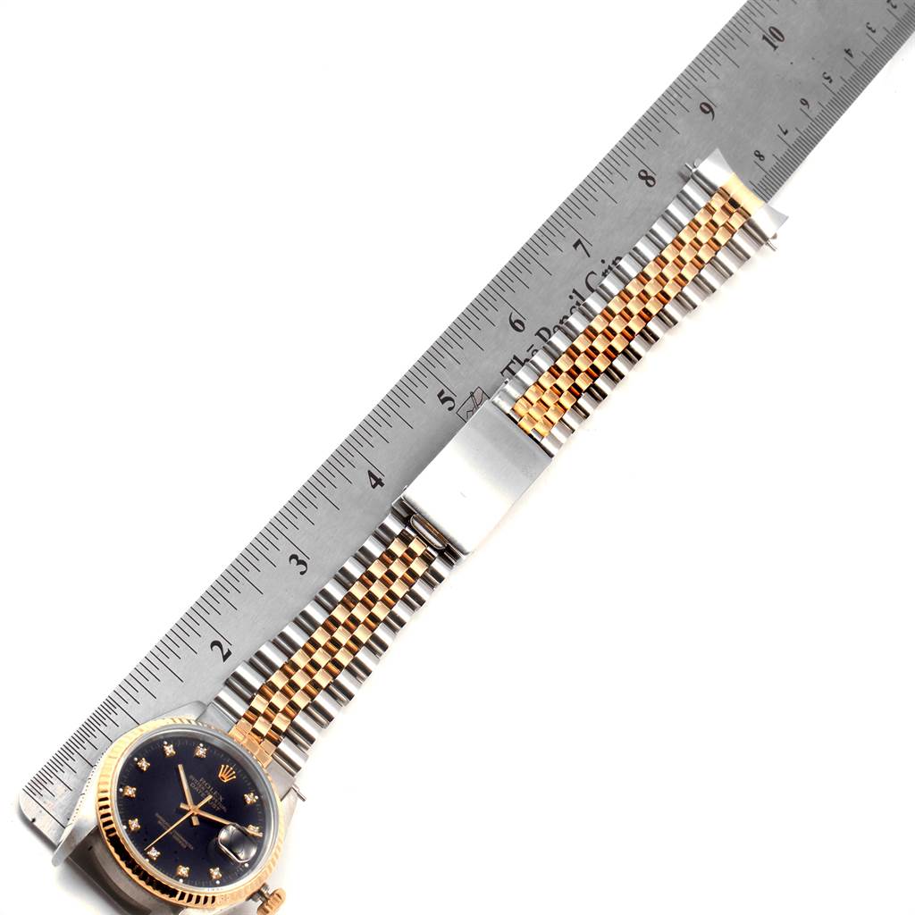 The image shows a top-down view of a Rolex Datejust 16233 Men's Steel and Gold (two tone) Black Dial 16233 Men's Steel and Gold (two tone) Black Dial watch, including its face and Jubilee bracelet, next to a ruler for measurement.