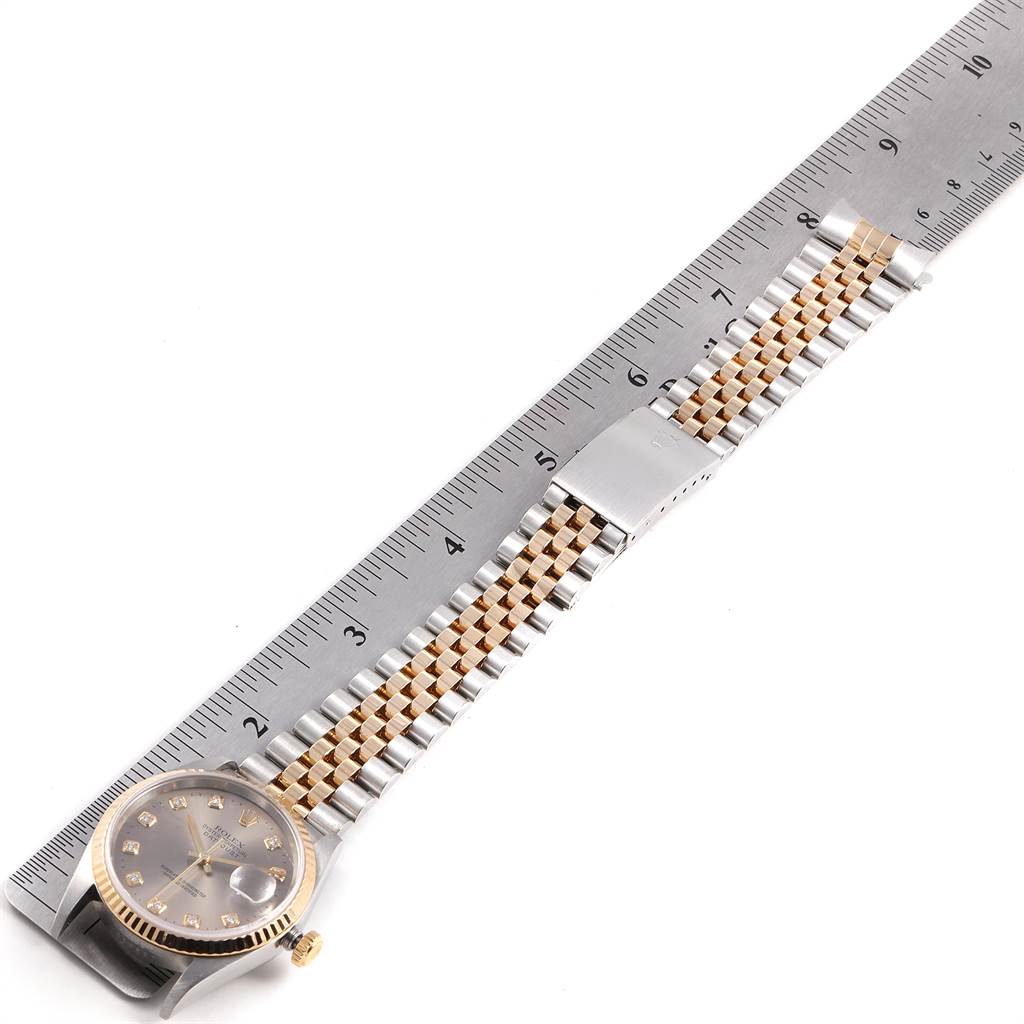 The Rolex Datejust 16233 Men's Steel and Gold (two tone) Silver Dial 16233 Men's Steel and Gold (two tone) Silver Dial watch is shown from an overhead angle, displaying its bracelet, dial, and part of the clasp alongside a ruler.